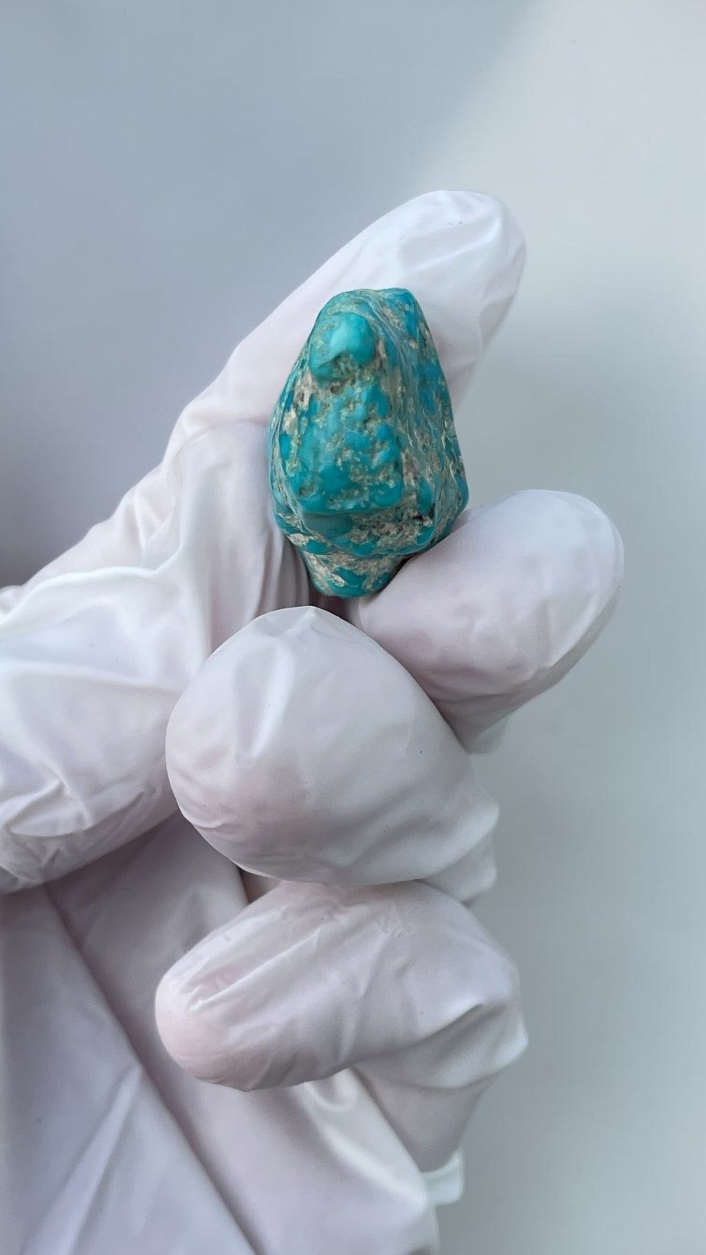 End view of polished Leadville turquoise specimen held in a gloved hand for scale