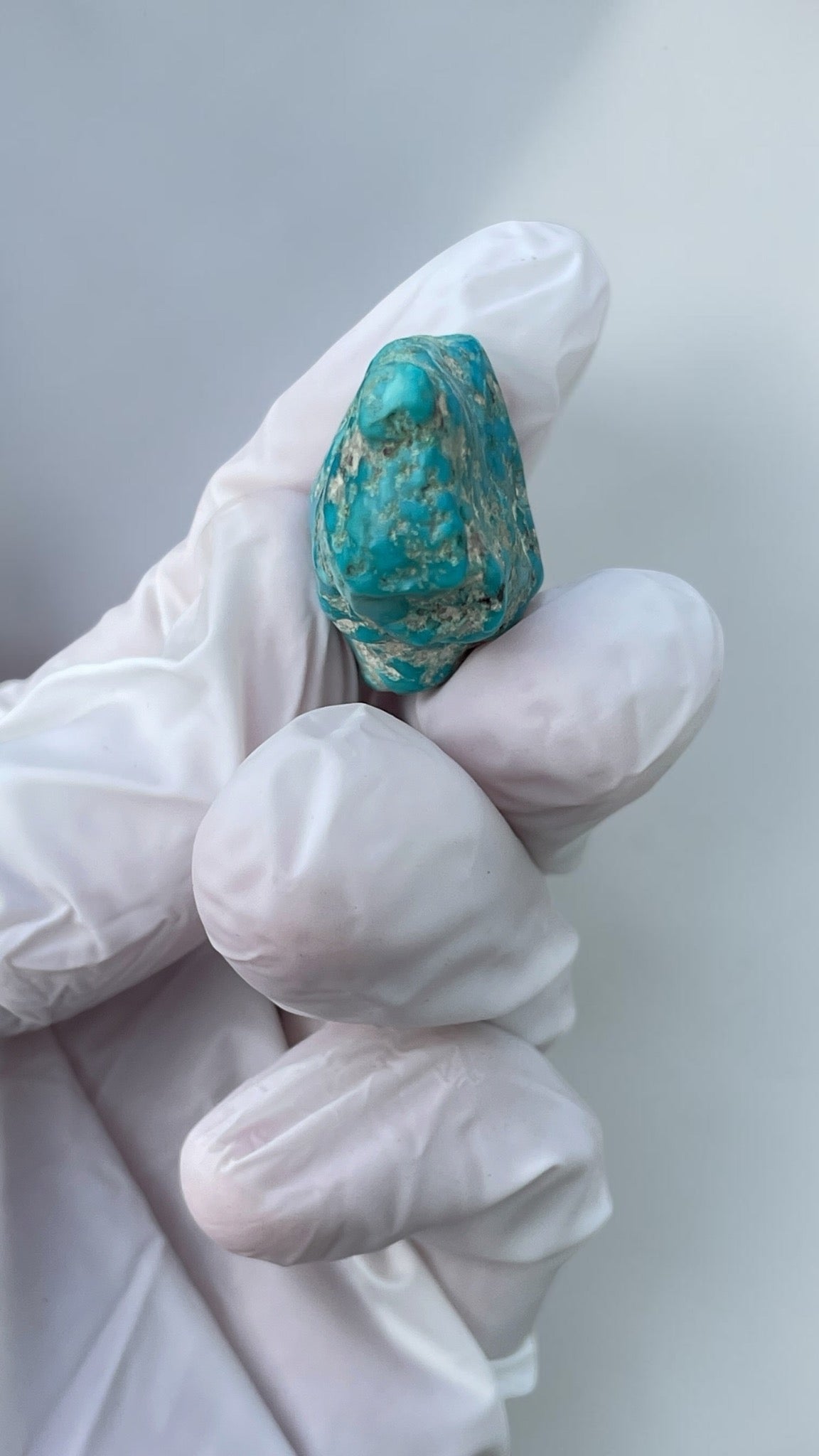 End view of polished Leadville turquoise specimen held in a gloved hand for scale