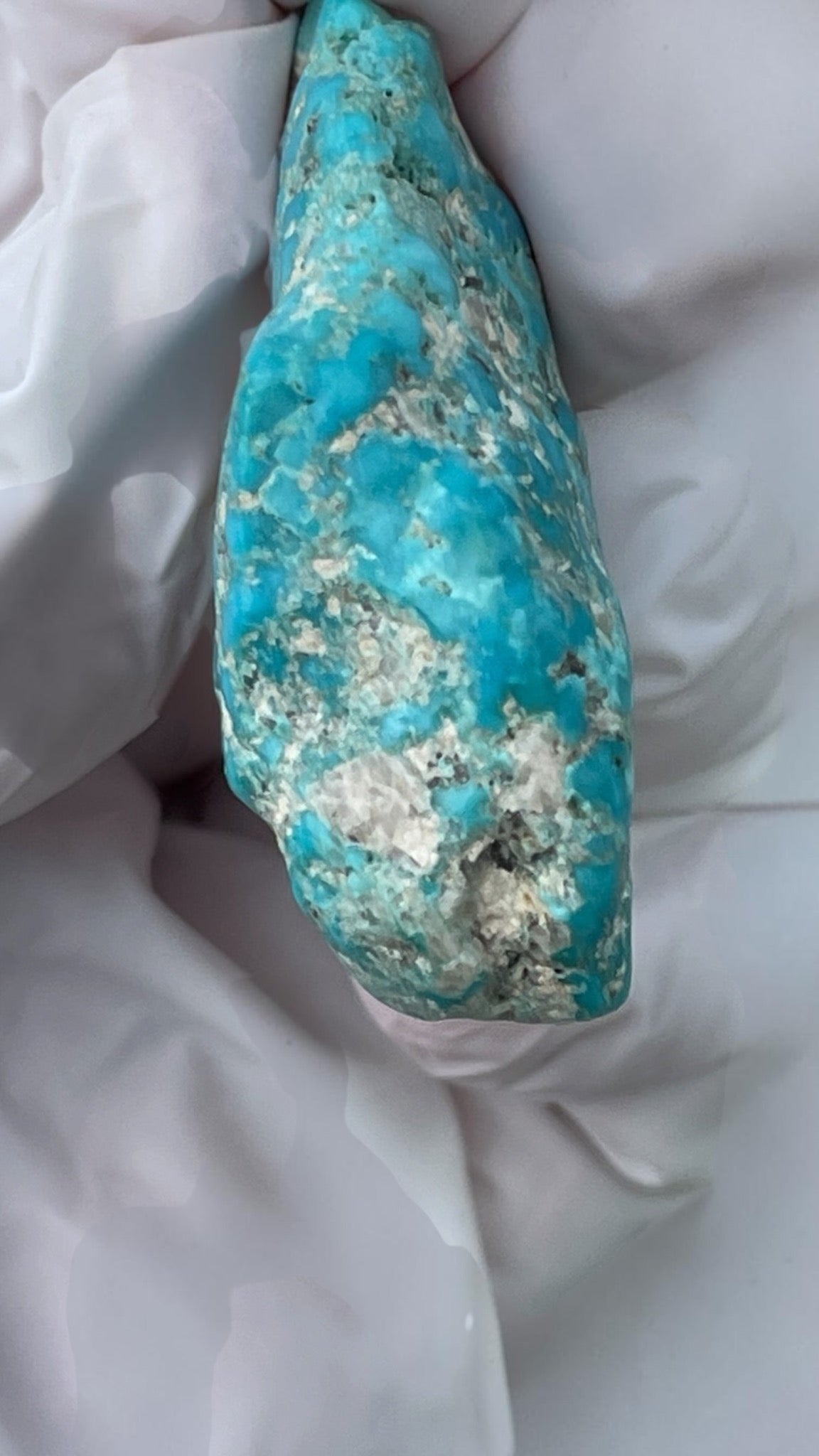 Side view of vivid blue polished Leadville turquoise specimen held for scale